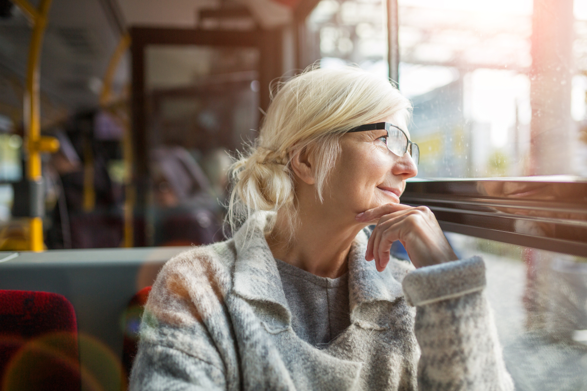 Seniorka w okularach sieci zadowolona w autobusie komunikacji miejskiej, patrząc przez szybę