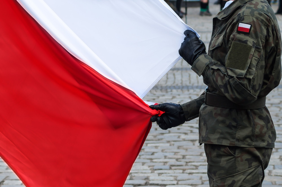 Polski żołnierz bez broni trzyma dużą flagę Polski