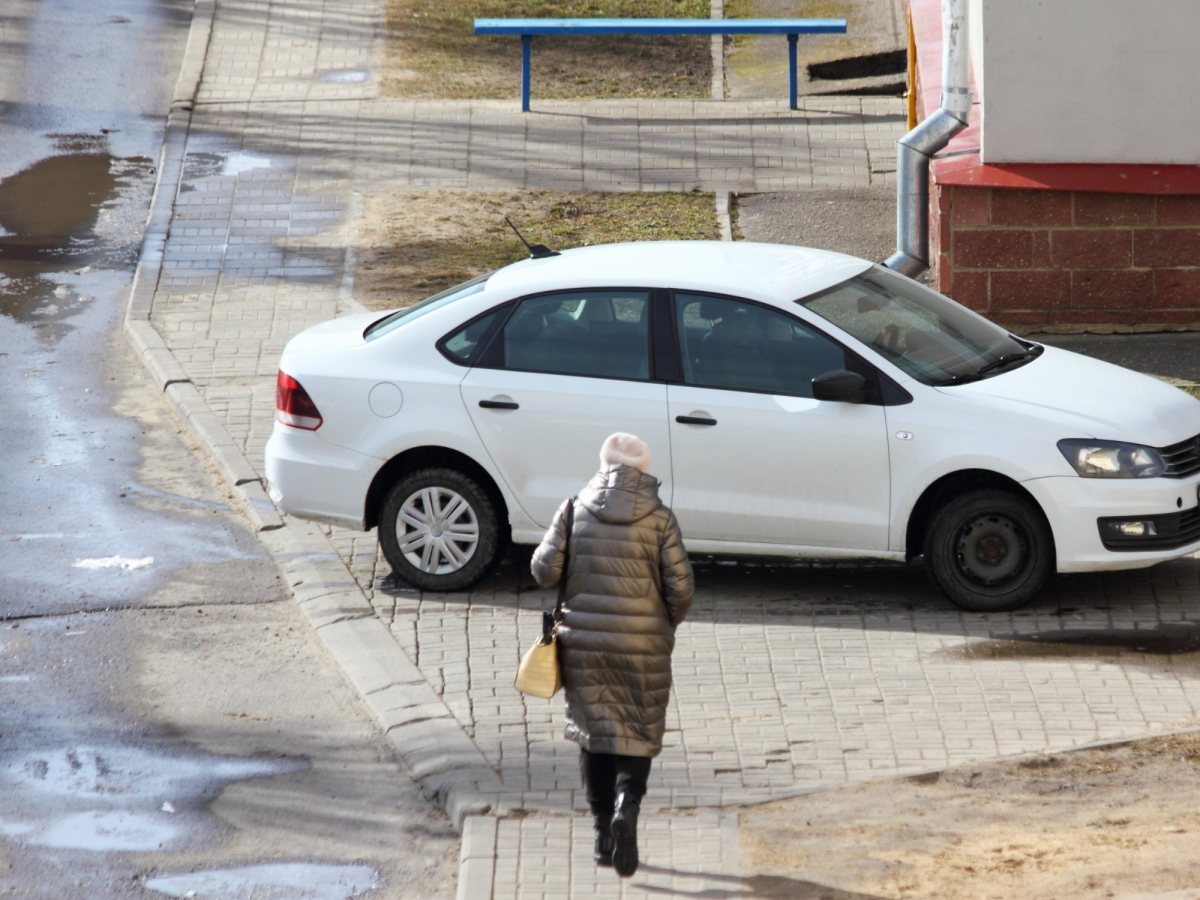 Kobieta chce przejść przez chodnik, który zajęło zaparkowane auto