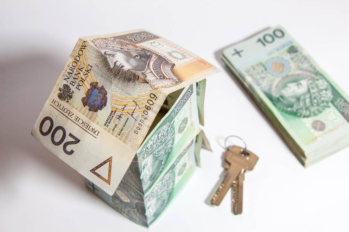 domek ułożony z polskich banknotów, obok klucze do mieszkania i stos banknotów