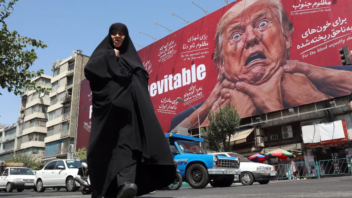 Kobieta w czarnym czadorze idzie ulicą miasta, w tle widać antyamerykański billboard propagandowy w Teheranie, stolicy Iranu, na którym widnieje wizerunek prezydenta USA Donalda Trumpa.
