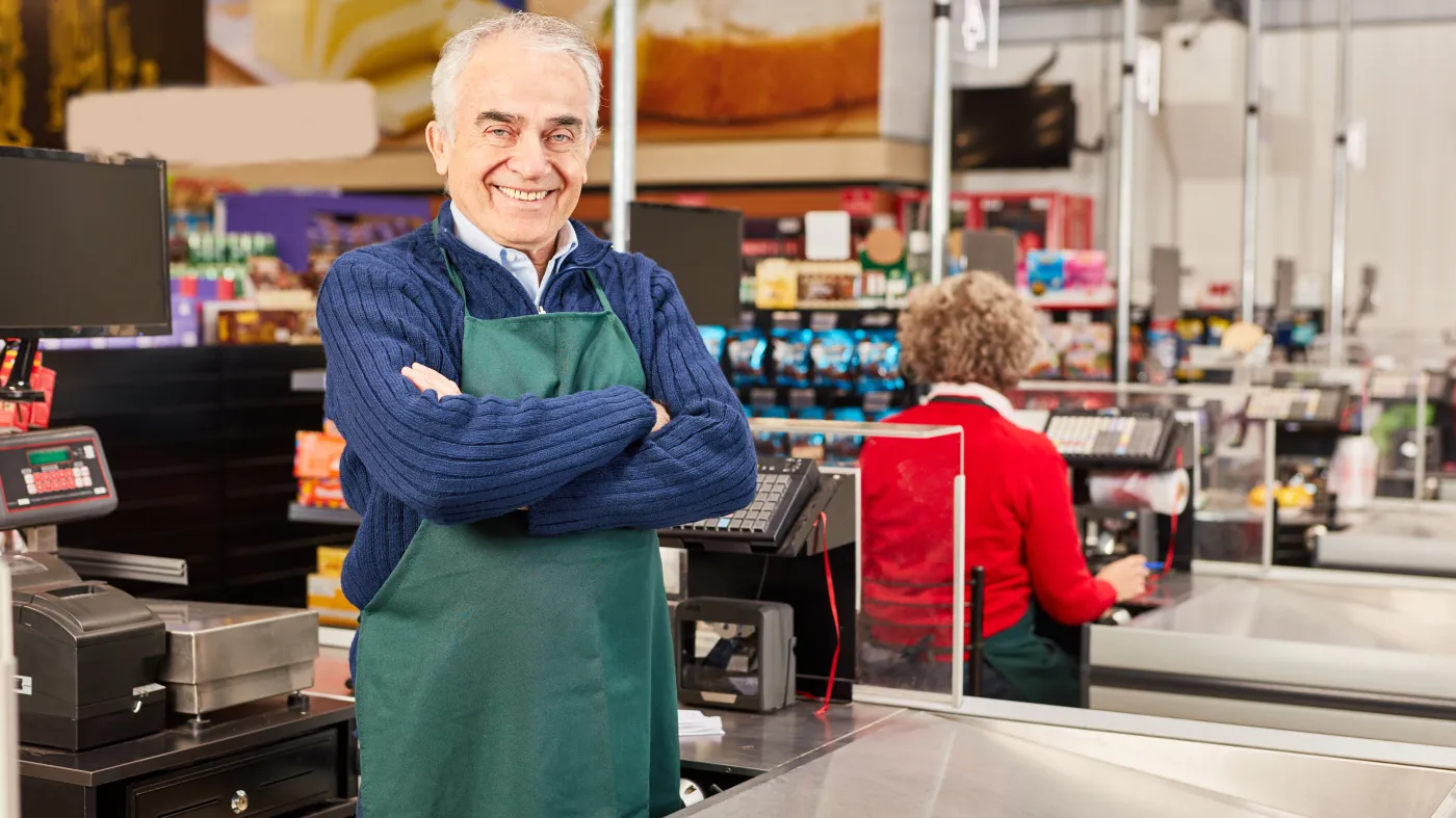 Senior,As,A,Cashier,Stands,With,Folded,Arms,At,The