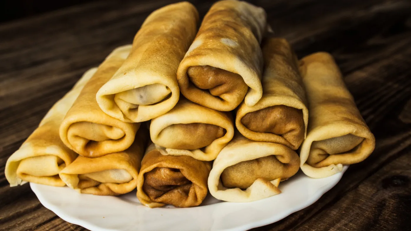 Stuffed,Crepe,Stacked,On,White,Plate,Wooden,Background