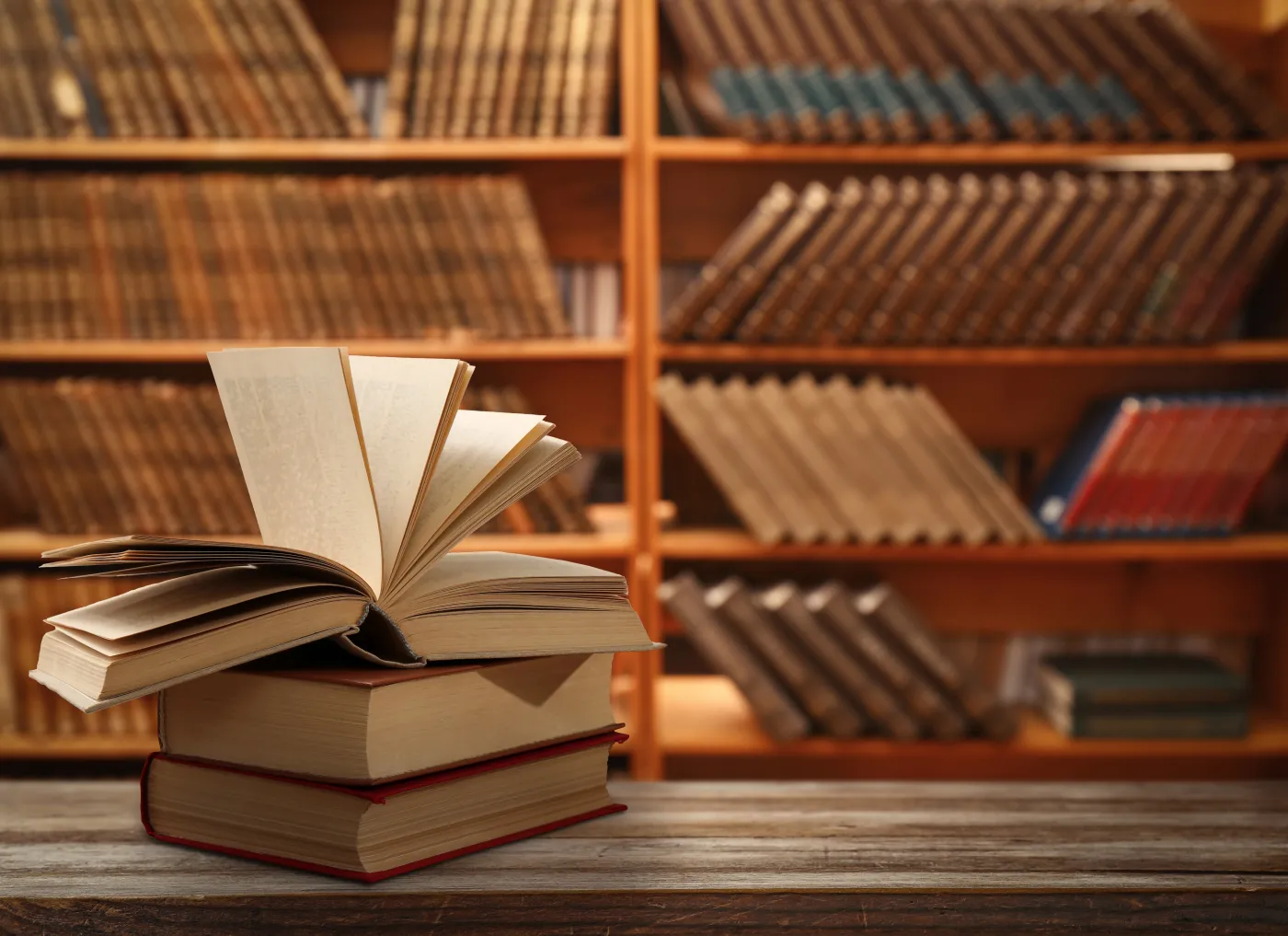 Books,On,Wooden,Table,Against,Shelves,In,Library.,Space,For