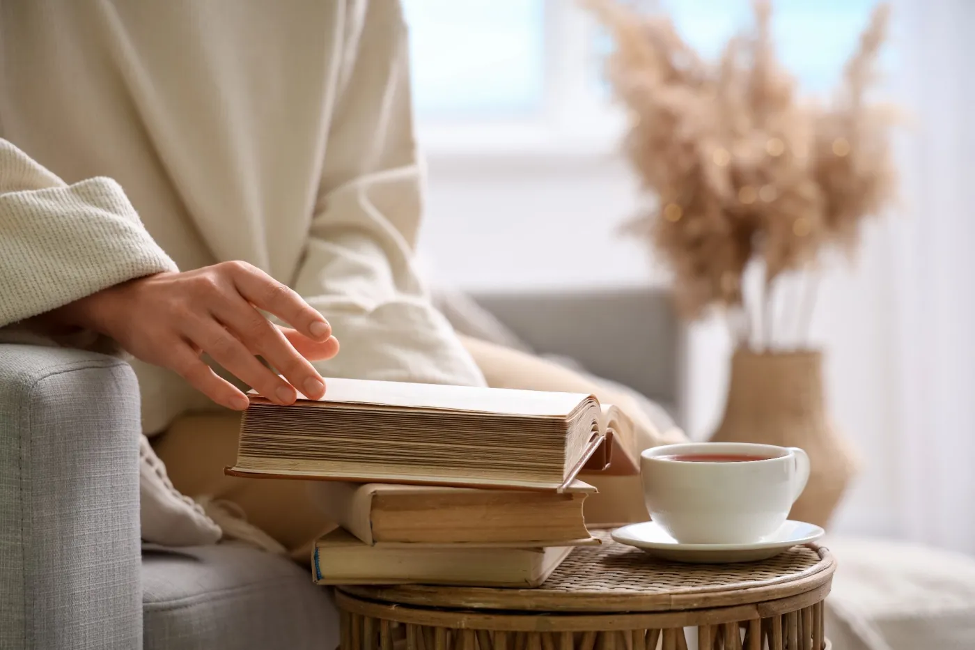 Young,Woman,Taking,Book,From,Stack,On,Table,At,Home,