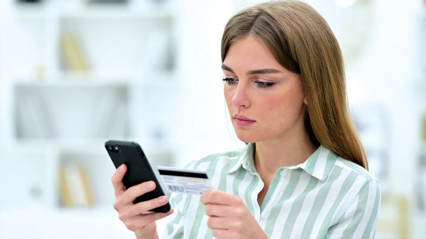 Kobieta trzyma kartę płatniczą i telefon - Rzecznik Finansowy ostrzega przed oszustwem na nieaktywną kartę