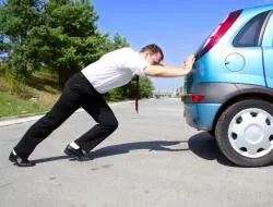 Mężczyzna pcha zepsuty samochód. fot. shutterstock.com