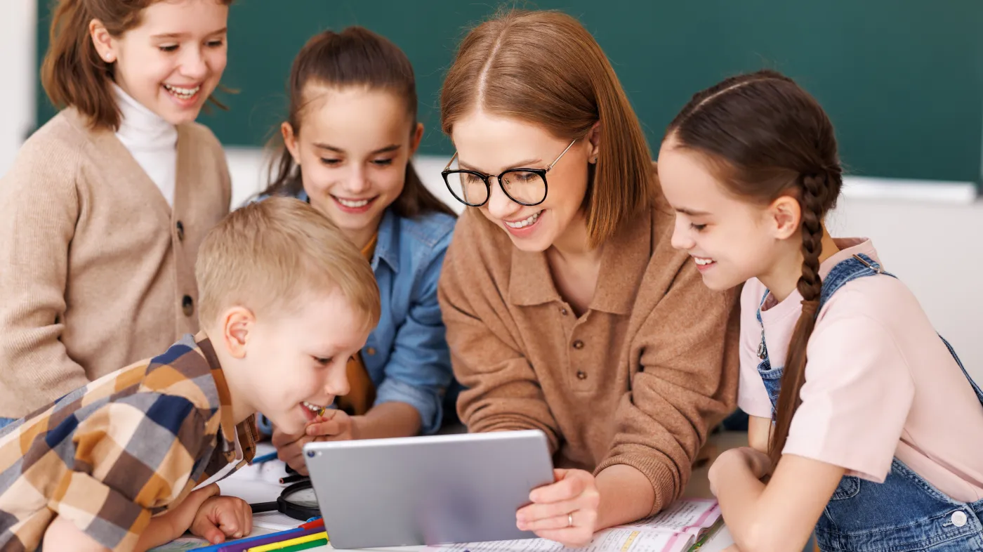 Happy,Female,Tutor,And,Optimistic,Children,Smiling,And,Watching,Video