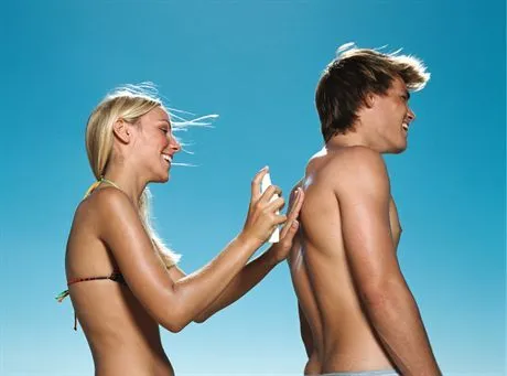 Woman spraying sun cream on boyfriends back --- Image by  Image SourceCorbis
