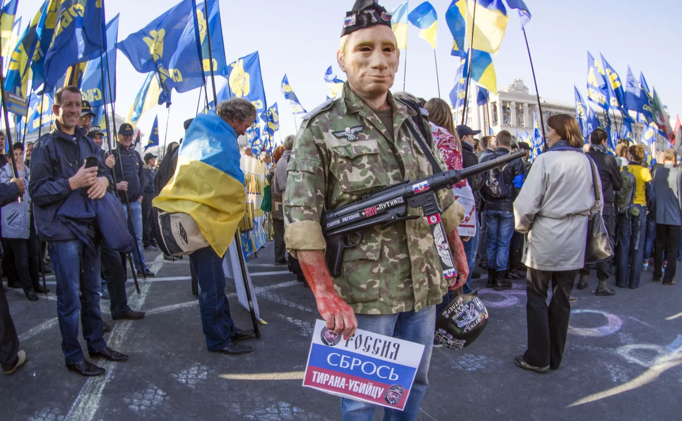 Mężczyzna w masce Władimira Putina, z pistoletem maszynowym i krwią na dłoniach na demonstracji w Kijowie
