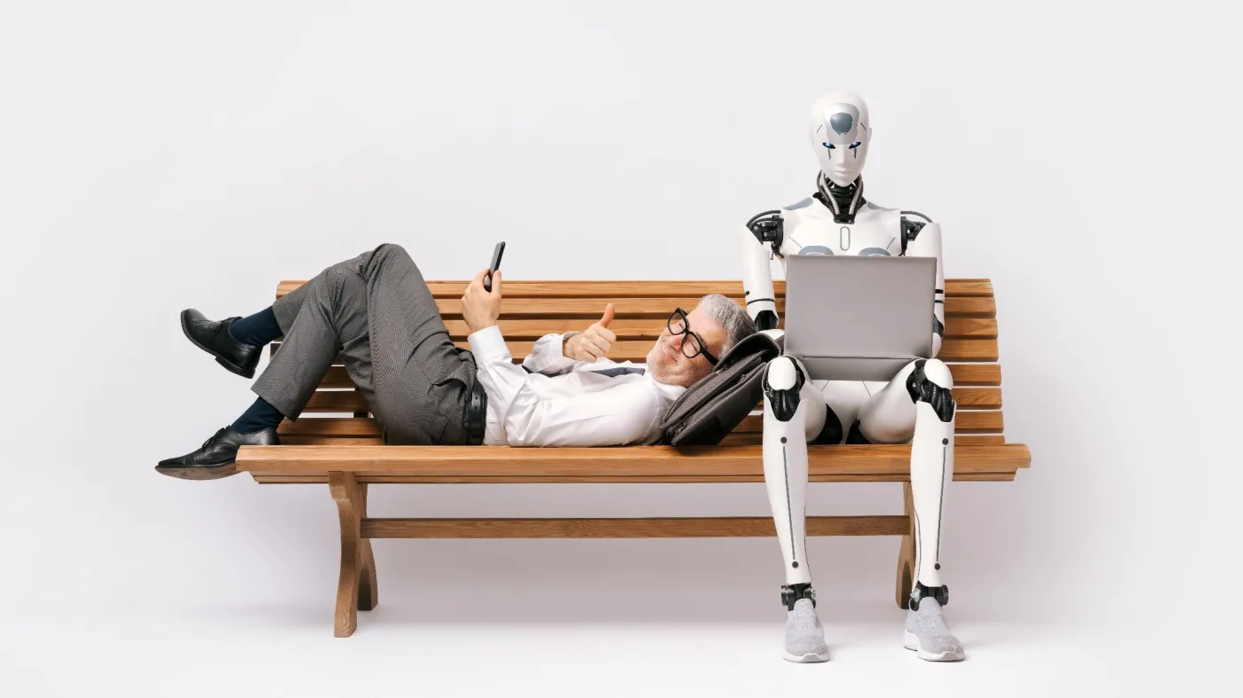 pracownik w białej koszuli leży na ławce zadowolony i korzysta ze smartfona, a obok niego na laptopie pracuje robot