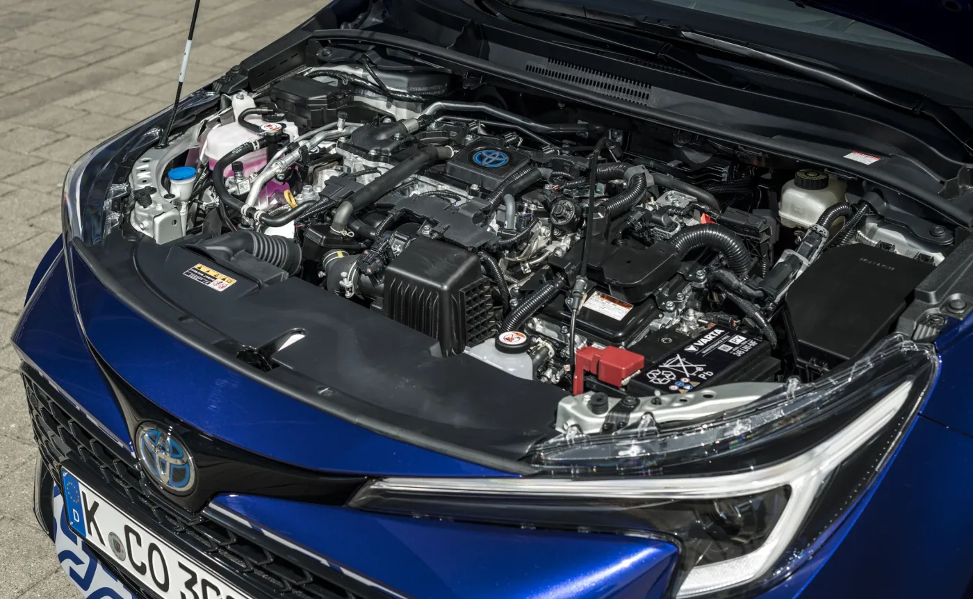 Otwarta komora silnika hybrydowej Toyoty Corolli w niebieskim kolorze lakieru, widoczne logo marki z niebieską poświatą oraz elementy jednostki napędowej