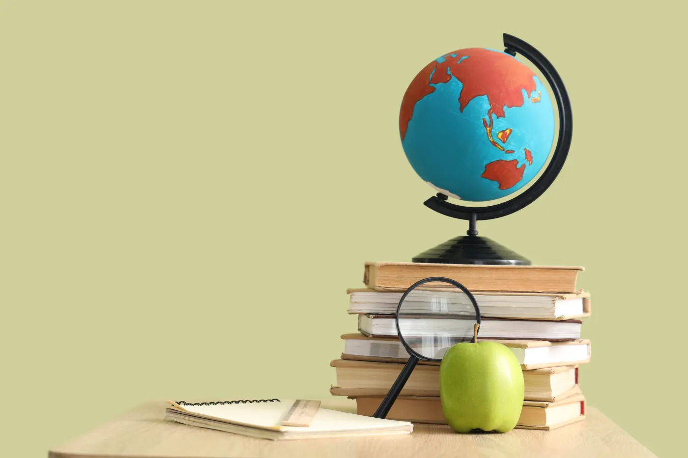 Globe,With,Books,,Magnifier,And,Apple,On,Desk,Against,Green