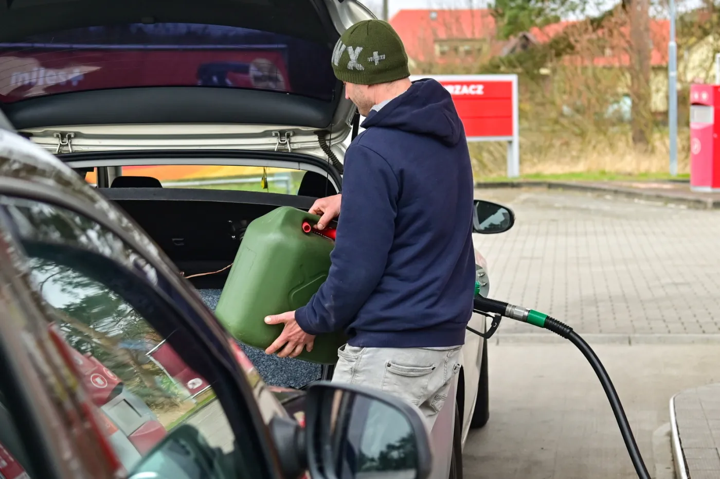 Kierowca tankuje paliwo do dużego zielonego kanistra w bagażniku samochodu na polskiej stacji benzynowej