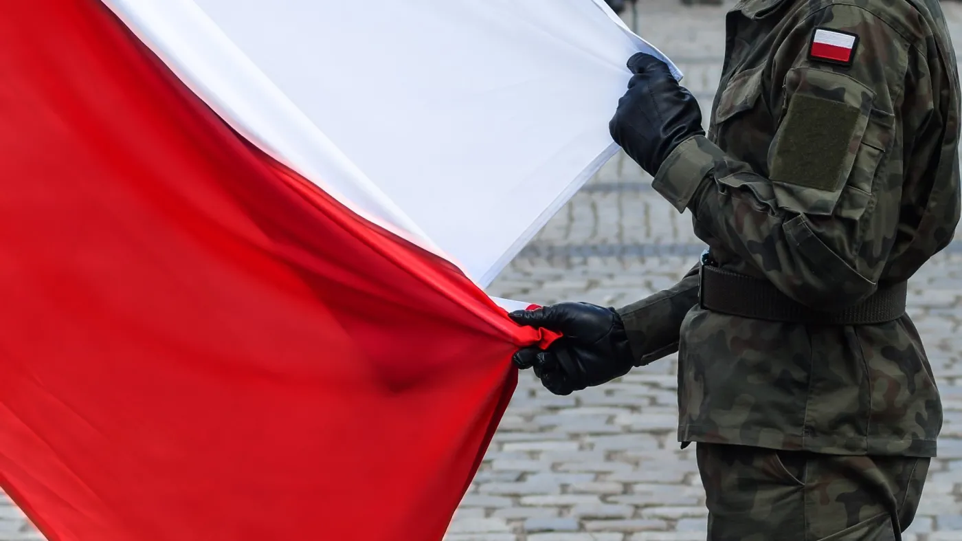Polski żołnierz bez broni trzyma dużą flagę Polski