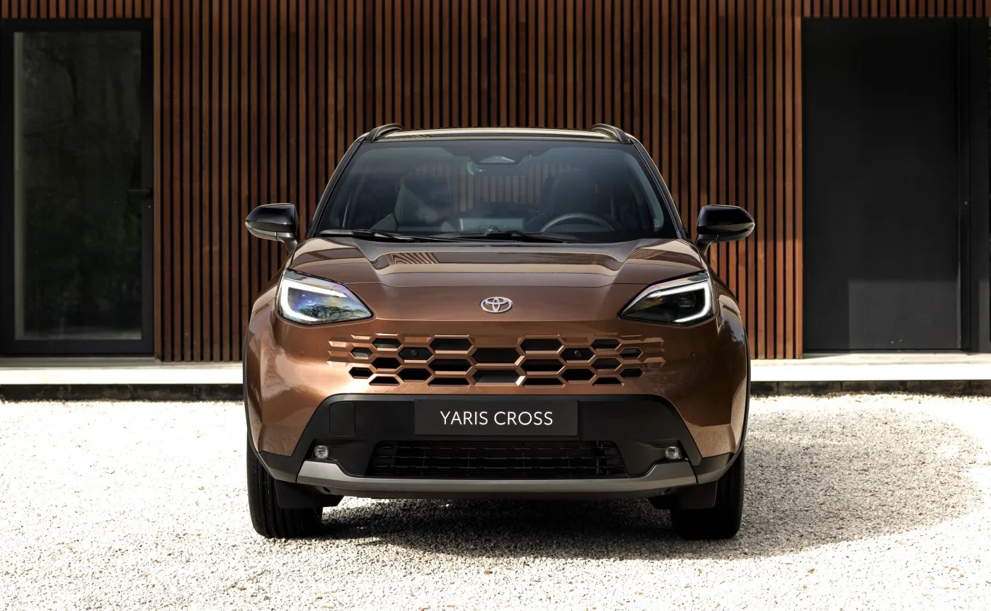 Nowa Toyota Yaris Cross w kolorze Precious Bronze z nowym grillem i reflektorami LED na tle nowoczesnego budynku