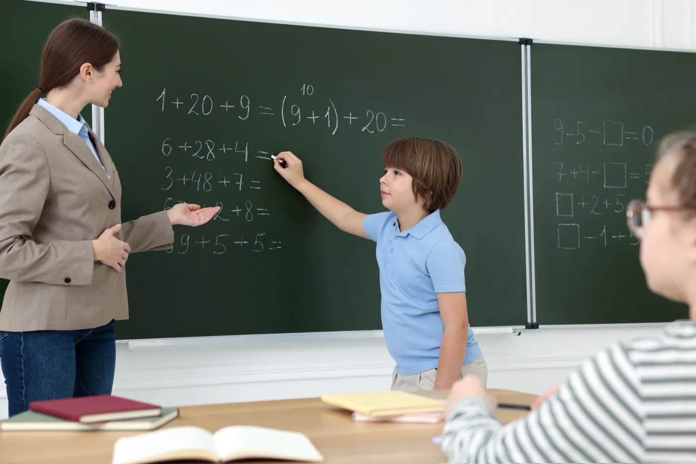 Schoolboy,Doing,Math,On,Chalkboard,And,Teacher,In,Classroom
