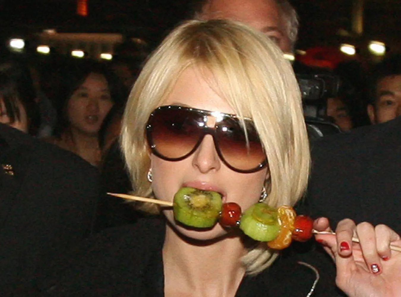 US socialite Paris Hilton C is escorted by bodyguards as she eats Chinese candied fruit during a tour on the historic Bund area of Shanghai, 22 November 2007.  Hilton is in China on a four day visit to present awards at the  quot;2007 MTV Style Gala quot; ceremony.      AFP PHOTOMark RALSTON
