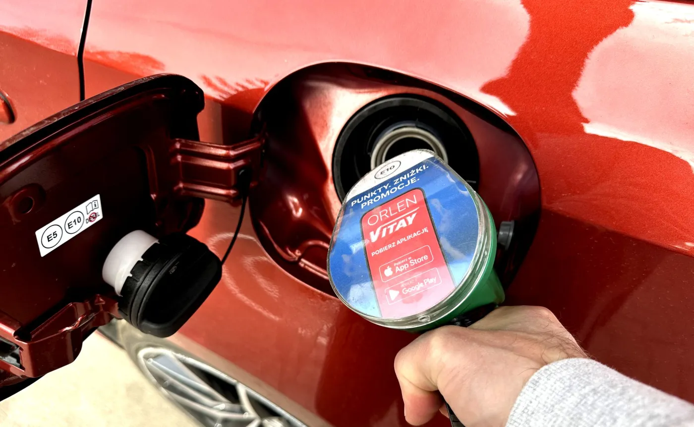 Bliskie ujęcie dłoni trzymającej pistolet do tankowania paliwa na stacji Orlen, włożony do wlewu czerwonego samochodu
