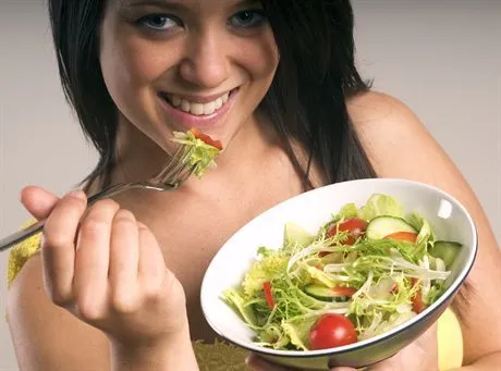 Young woman stood with a bowl of mixed salad containing iceberg lettuce,cherry tomatoes,cucumber,frisee,radish and sliced red peppers.