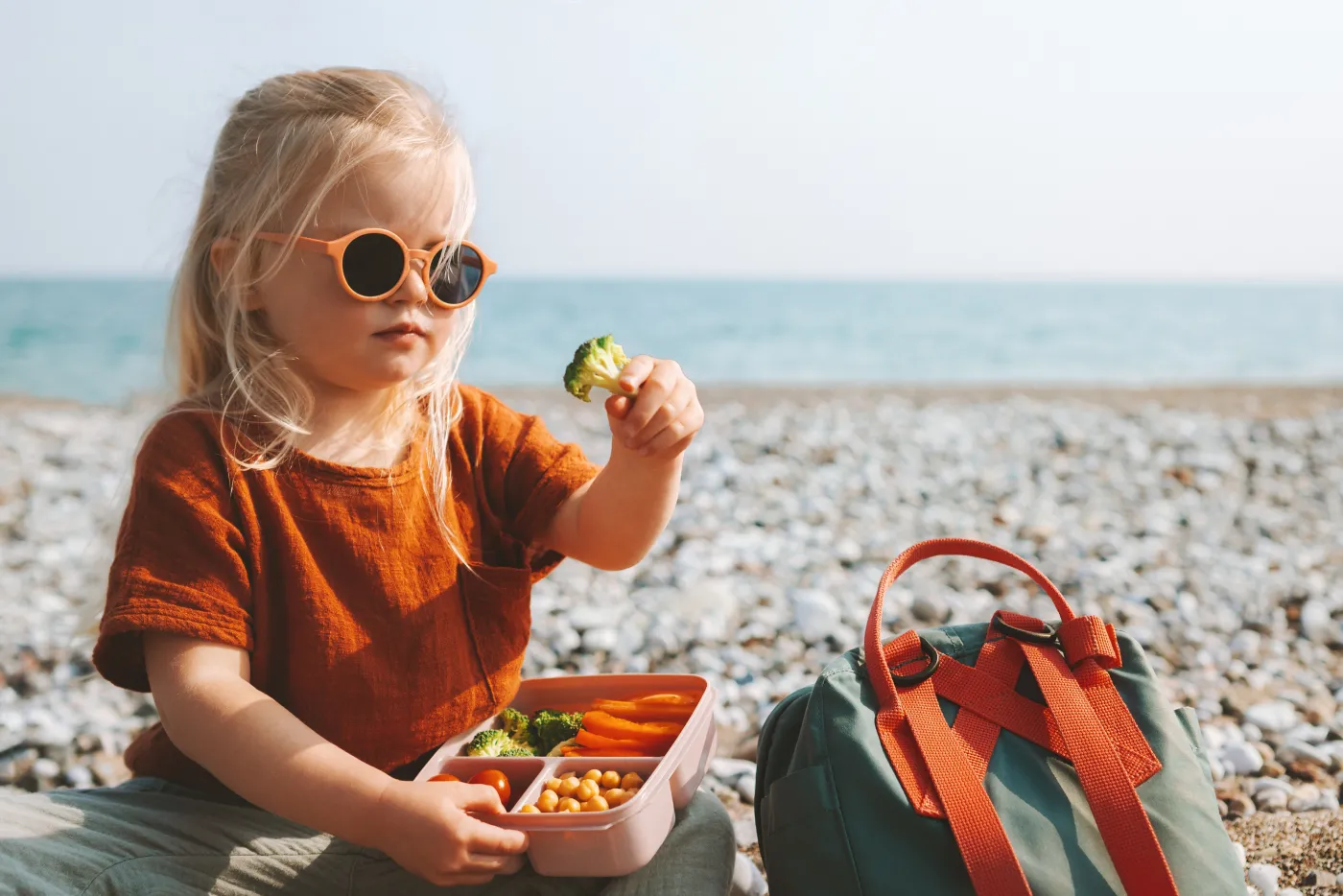 Child,Girl,Eating,Broccoli,With,Lunch,Box,Picnic,On,Beach