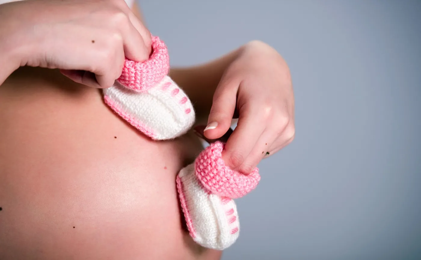 Kobieta w ciąży trzyma małe buciki na brzuchu