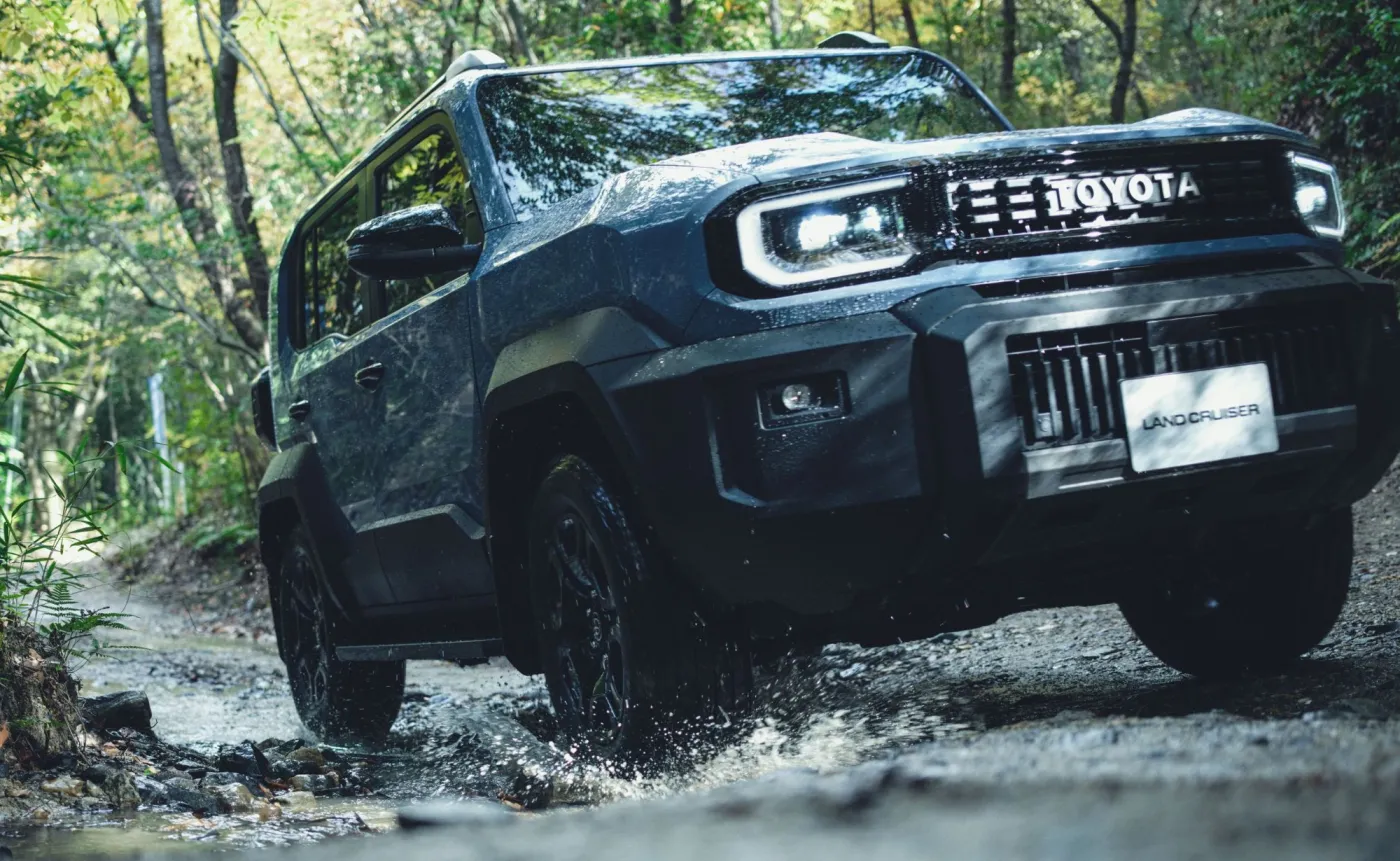 Nowa Toyota Land Cruiser FJ jedzie przez wodny bród w lesie, widoczny przód auta z napisem Toyota i Land Cruiser na tablicy rejestracyjnej