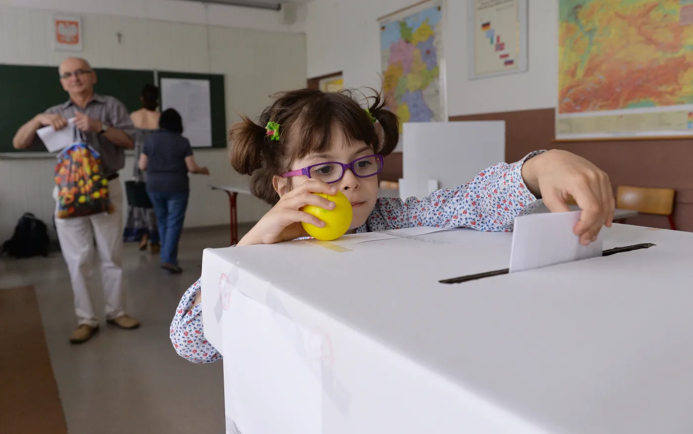 Głosowanie w Obwodowej Komisji ds. Referendum nr 47. Mieszkańcy Krakowa uczestniczą 25 bm. w lokalnym referendum, w którym wypowiadają się czy chcą organizacji Zimowych Igrzysk Olimpijskich w Krakowie w 2022 roku. Dzieci "pomagają" rodzicom we wrzuceniu karty do głosowania do urny