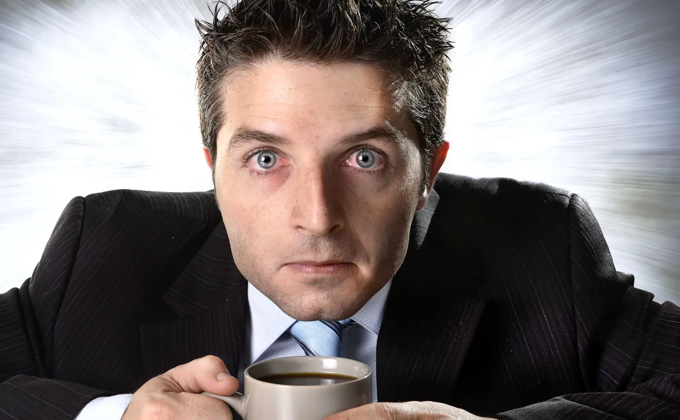 Mężczyzna z przekrwionymi oczami siedzi nad kubkiem kawy