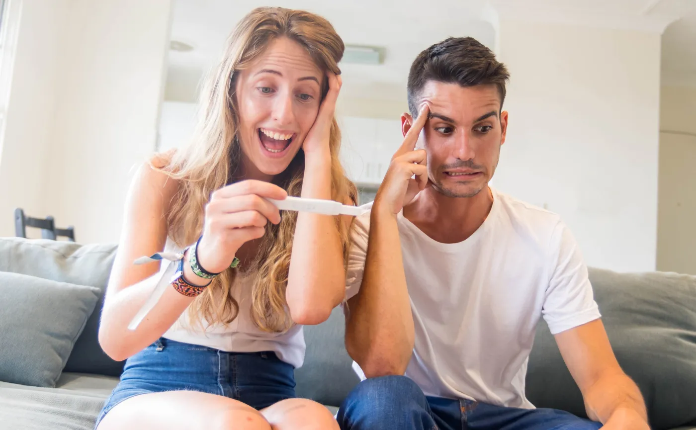 Kobieta patrzy na test ciążowy z radością, mężczyzna ma problem
