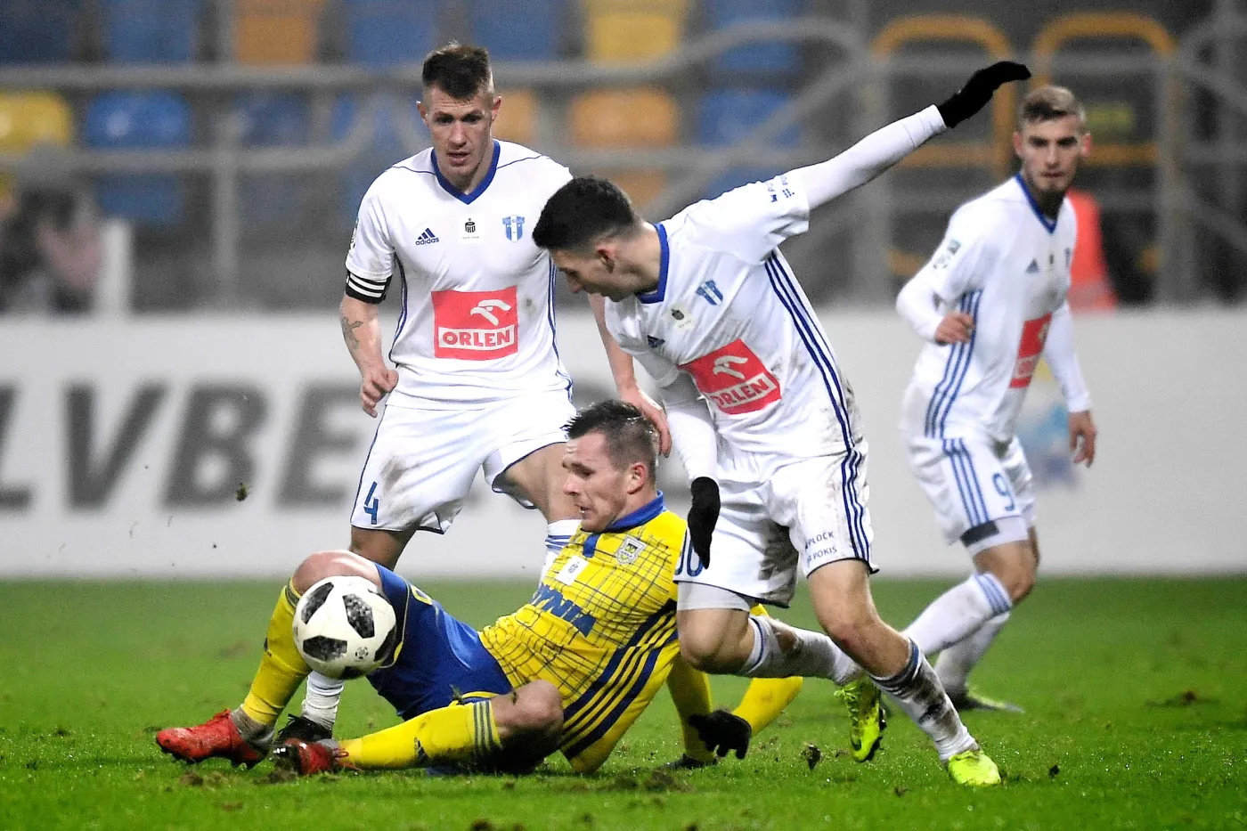 Zawodnik Arki Gdynia Adam Deja (dół) oraz Damian Szymański (L) i Jakub Łukowski (P) z Wisły Płock