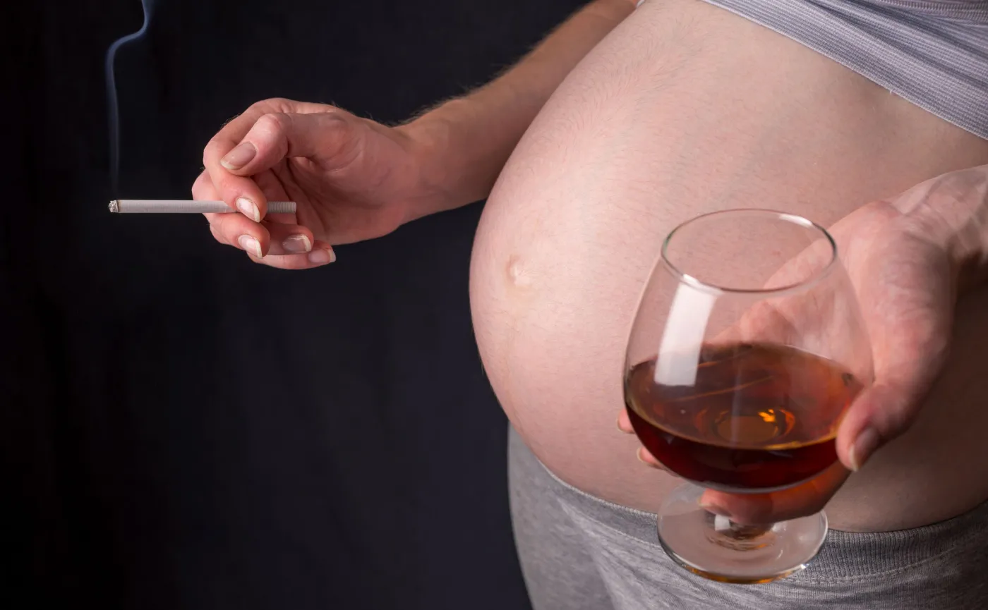Kobieta w ciąży z kieliszkiem alkoholu i papierosem