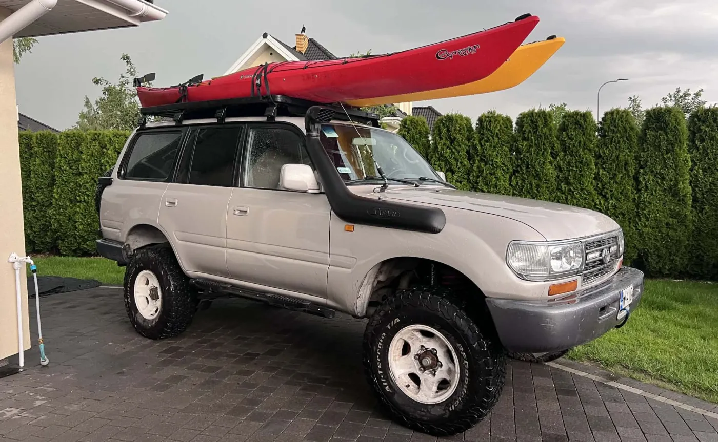 Terenowa Toyota Land Cruiser z dwoma kolorowymi kajakami zamontowanymi na solidnym bagażniku dachowym przy użyciu pasów transportowych