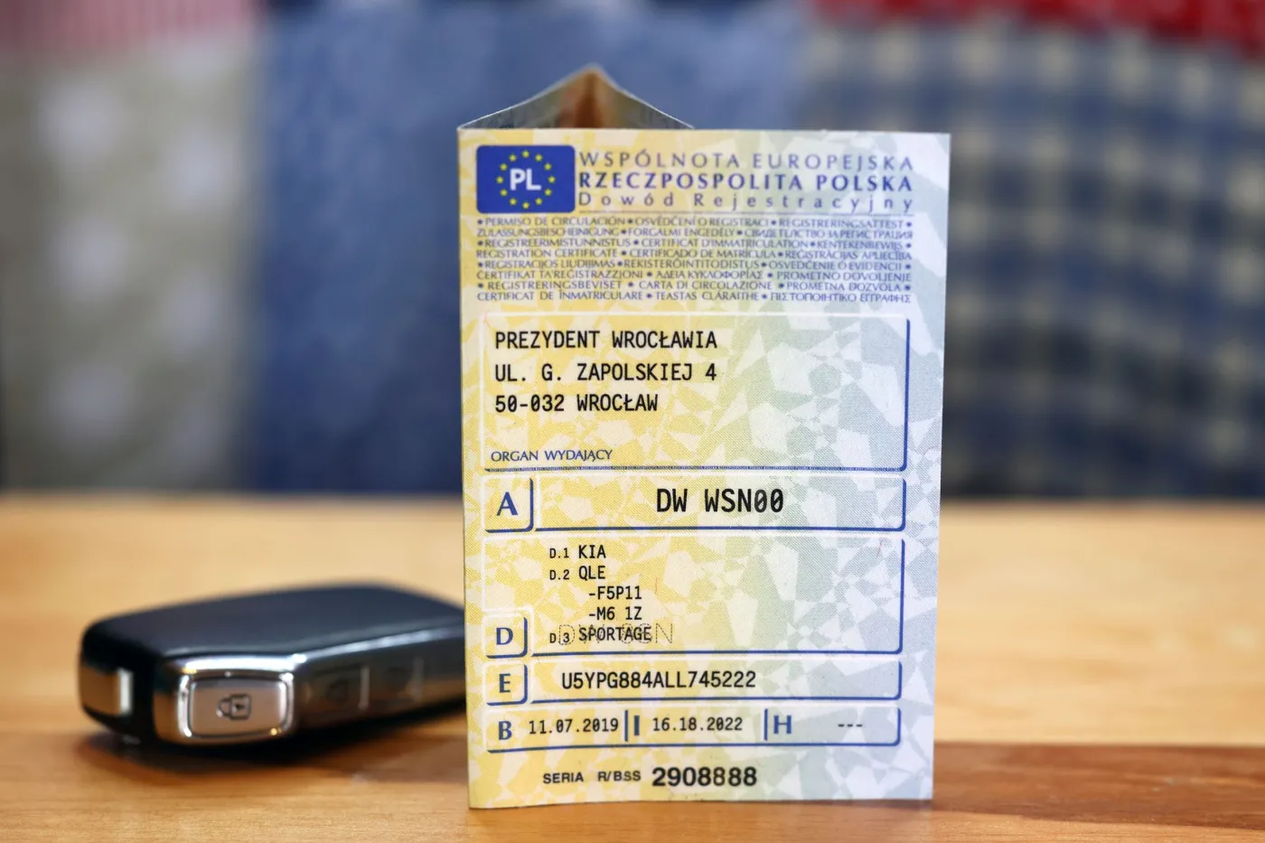 Papierowy dowód rejestracyjny stojący na drewnianym stole obok kluczyka samochodowego – ilustracja do artykułu o cyfryzacji dokumentów komunikacyjnych