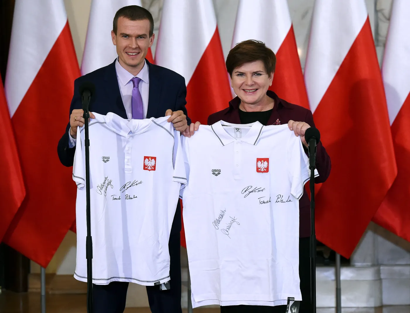 Premier Beata Szydło (P) i minister sportu i turystyki Witold Bańka (L) pozują do zdjęcia z pamiątkowymi kuszulkami podczas spotkania z medalistami mistrzostw Europy w pływaniu na krótkim basenie