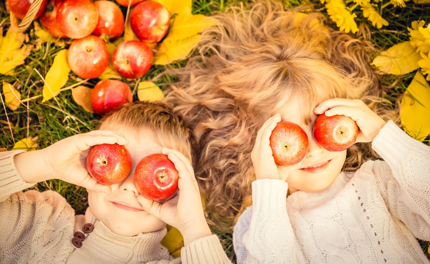 Dzieci leżą na liściach i trzymają jabłka