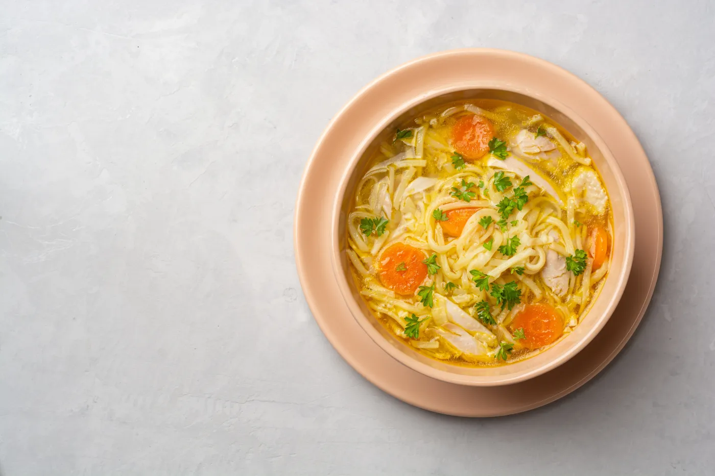 Chicken,Soup,With,Noodles,And,Vegetables,In,Bowl,On,Concrete
