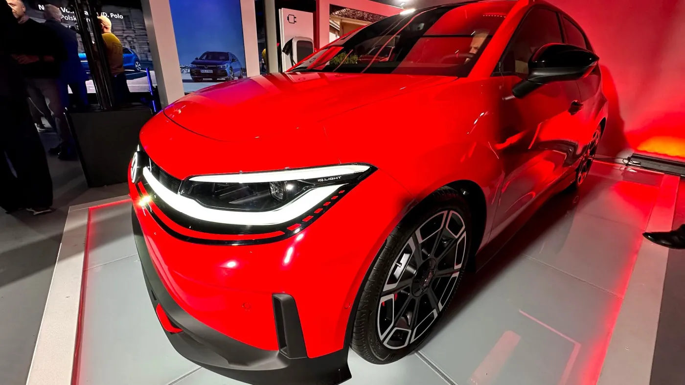 Nowy czerwony samochód elektryczny Volkswagen ID. Polo sfotografowany od przodu podczas oficjalnej premiery, widoczne nowoczesne reflektory LED i czarne felgi