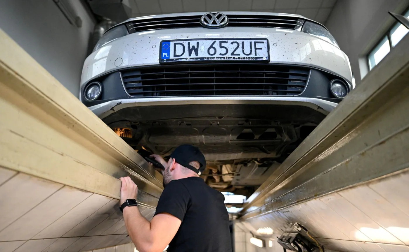 Badanie techniczne pojazdu na stacji kontroli pojazdów SKP. Diagnosta samochodowy w kanale sprawdza stan podwozia i układu wydechowego pod samochodem Volkswagen Touran. Nowe przepisy i procedury przeglądów aut w 2026 roku