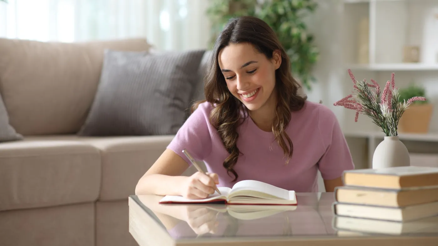 Happy,Woman,Writing,In,Paper,Agenda,Over,Coffee,Table,At