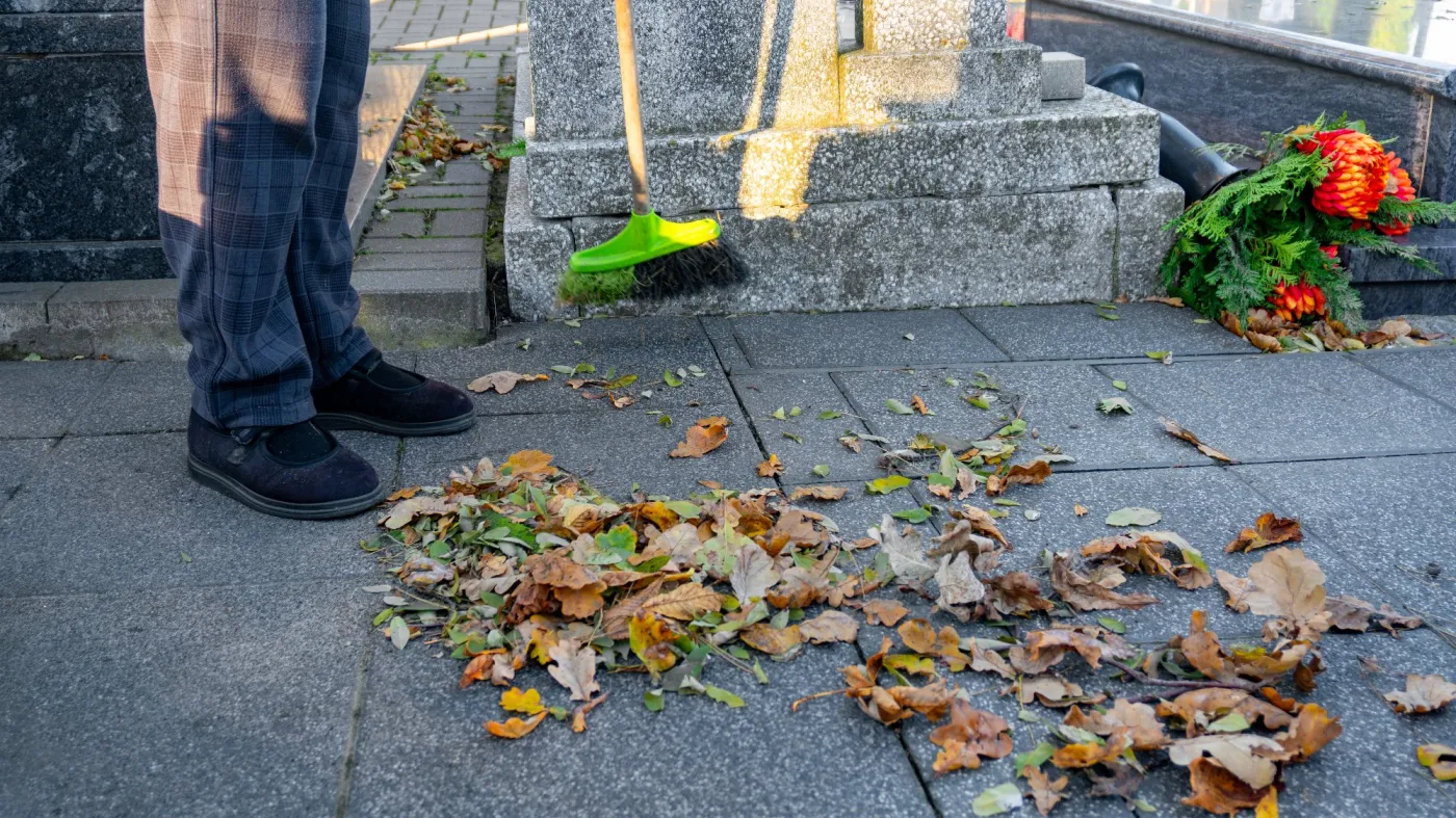 Zamiatanie liści podczas sprzątania grobu na cmenatarzu