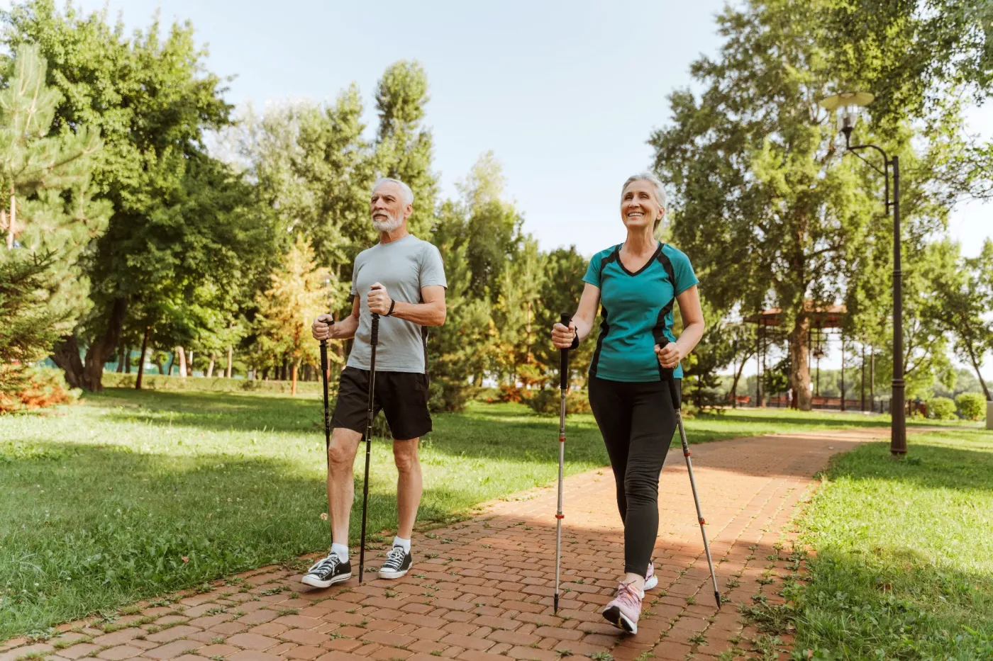 Zadowolona para seniorów na spacerze nordic walking w zielonym parku