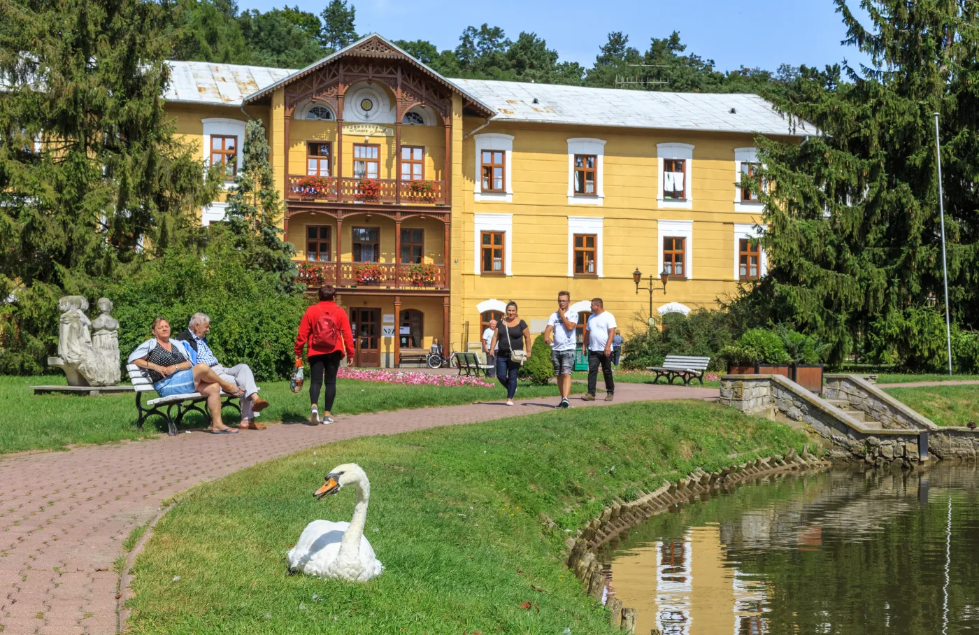 Kuracjusze spacerują po deptaku w sanatorium i podziwiają łabędzie