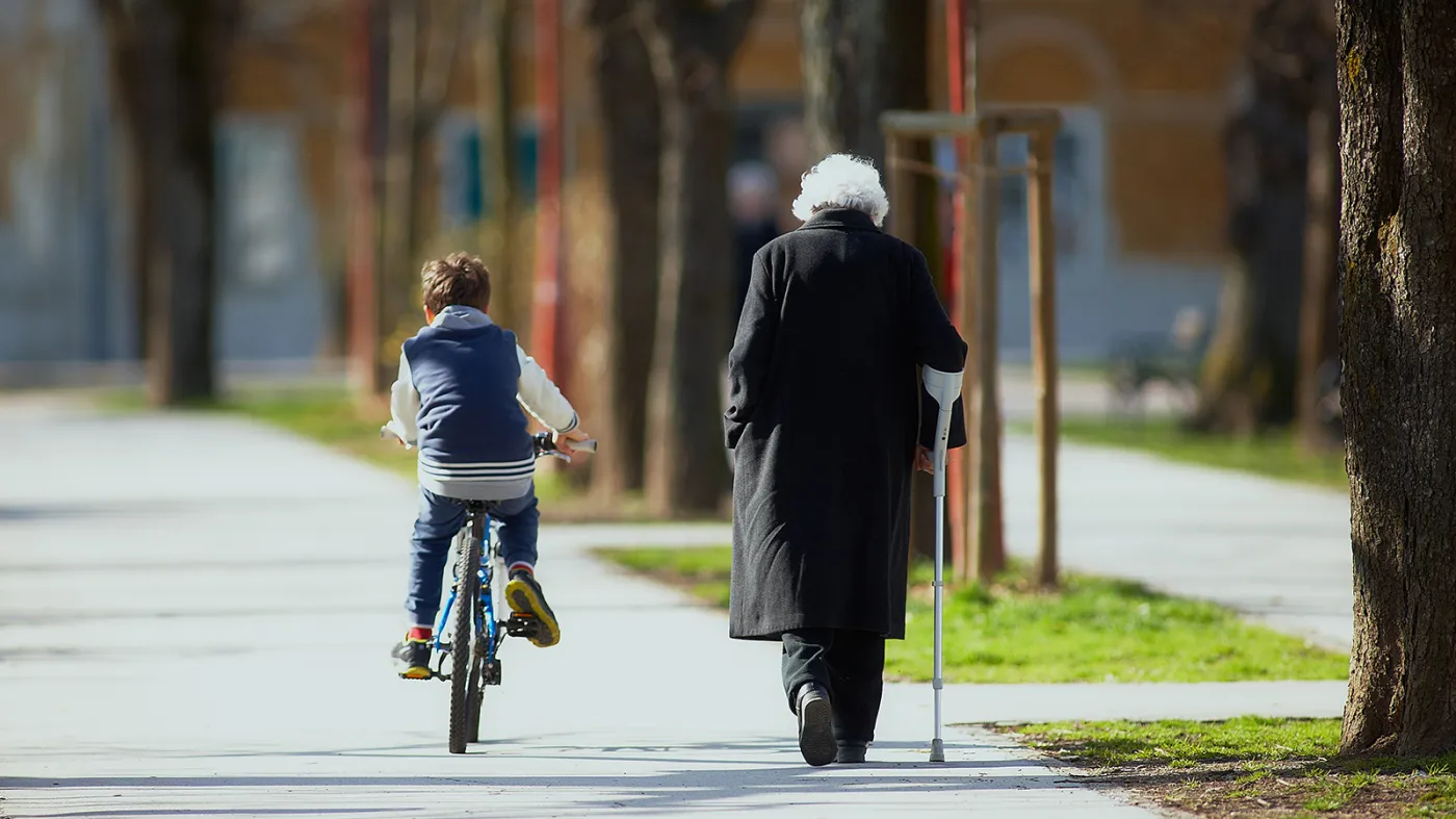 Starsza kobieta z laską i dziecko jadące na rowerze. Zmiany demograficzne w Polsce