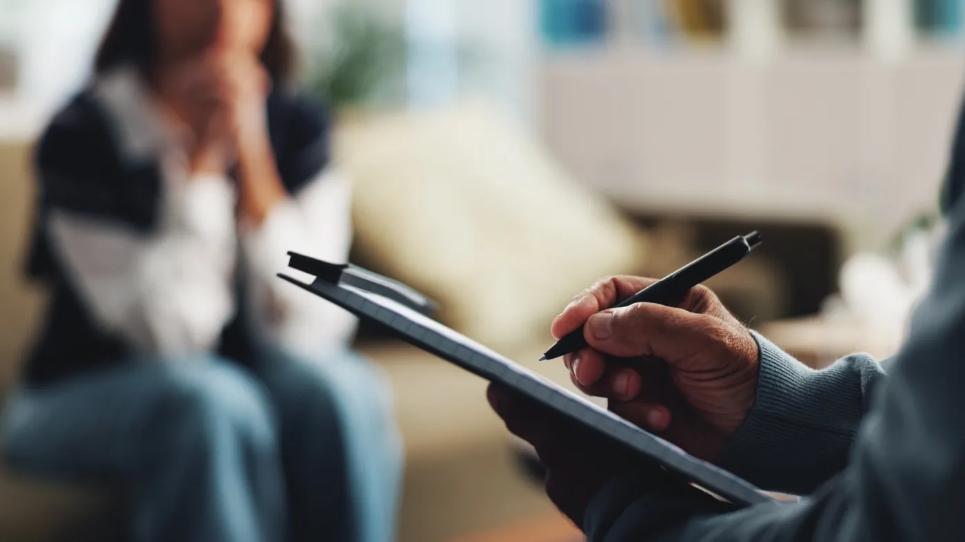 pacjent podczas porady psychologicznej w rozmytym tle, na pierwszym planie notes i długopis w dłoni