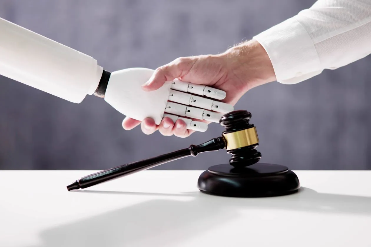 Człowiek podaje sobie rękę z robotem, na drugim planie znajduje się młotek sędziowski