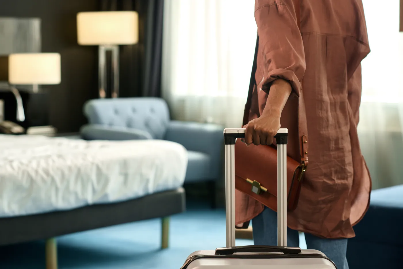 kobieta odwrócona tyłem w hotelowym pokoju z walizką w dłoni - odliczenie VAT przez branżę turystyczną