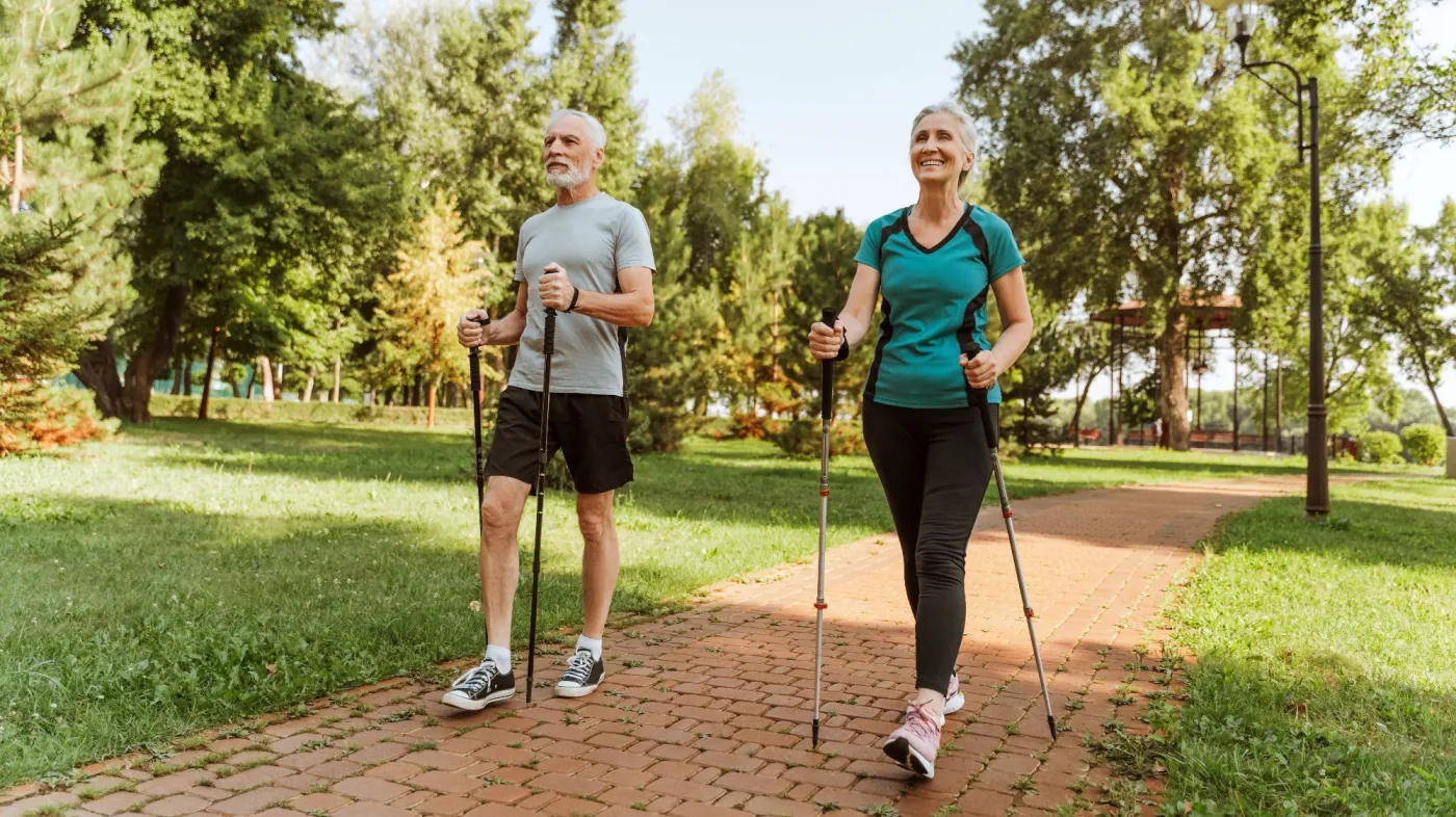 Zadowolona para seniorów na spacerze nordic walking w zielonym parku.