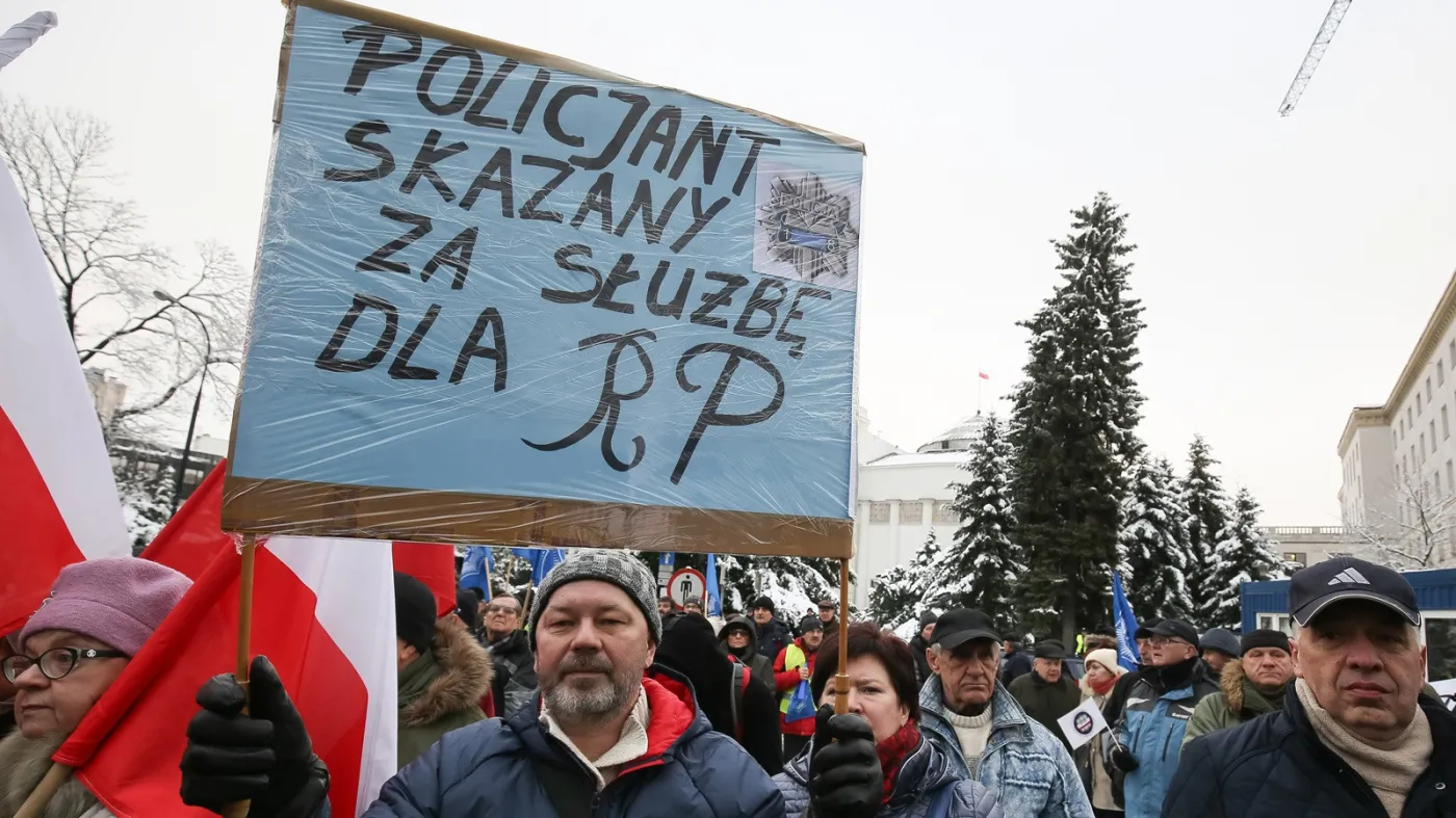 Uczestnicy protestu przed Sejmem z transparentem „Policjant skazany za służbę dla RP”